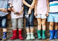 Kunterbunt gekleidete Kinder in Gummistiefeln stehen in einer Reihe, halten Lupen in den Händen und möchten mehr über Kunterbunt Second Hand herausfinden.